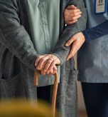 Close up hands of caregiver doctor helping old woman at private clinic. Close up of hands of nurse holding a senior patient with walking stick. Elder woman using walking cane at nursing home with nurse holding hand for support.